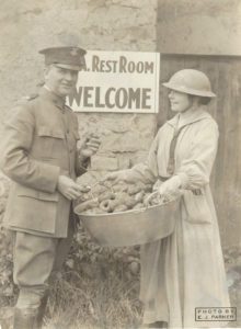A man in military uniform poses with a woman holding a tub of doughnuts
