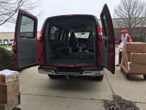 A red cargo van with man standing next to it. He is pulling a trolly full of boxes