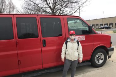 Person standing outside red cargo van. Person wears EDS hat and face mask