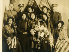 A group of men and women posing with US flags and a wreath decorated with glowers and doughnuts