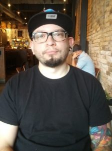 Man in black top with glasses seated