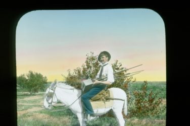 A man holding an old fashioned camera while sitting on the back of a mule