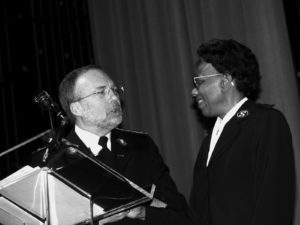 Photograph of a black woman wearing a Salvation Army uniform talking at a podium with a man also wearing a Salvation Army uniform