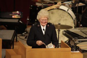 Photograph of Commissioner Eva Gaither preaching. She holds a bible and stands behind a large wood podium. Instruments from a band can be seen behind her. They include a bass drum and xylophone.