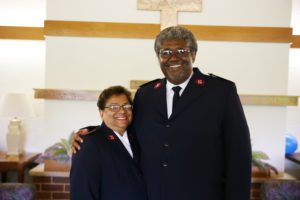 Photograph of Majors Stephen and Diane Harper. They are standing in front of a cross inside a church