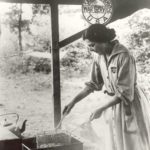Black and white photograph of a woman frying doughnuts in a WWI outdoor kitchen