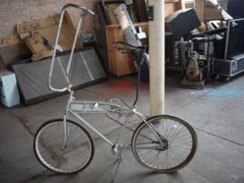 A photograph of a silver tall bike as found in an abandoned workroom