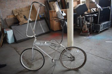 A photograph of a silver tall bike as found in an abandoned workroom