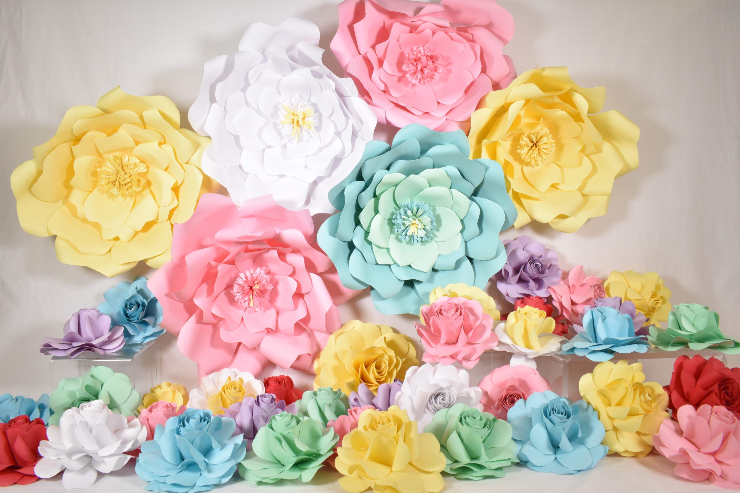 An arrangement of large and small paper flowers made from colored printer paper. They look like roses and are in white, yellow, blue, pink, green, purple and red.