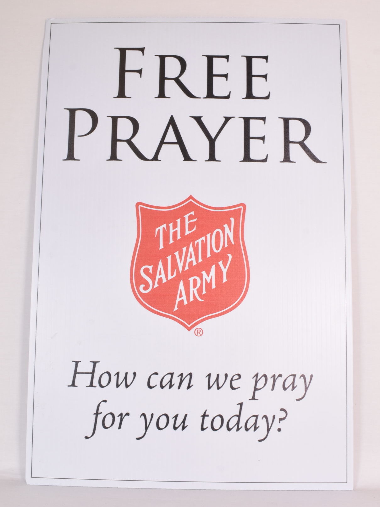 A white corrugated plastic sign with black text "Free Prayer. How can we pray for you today" and the Red Shield logo