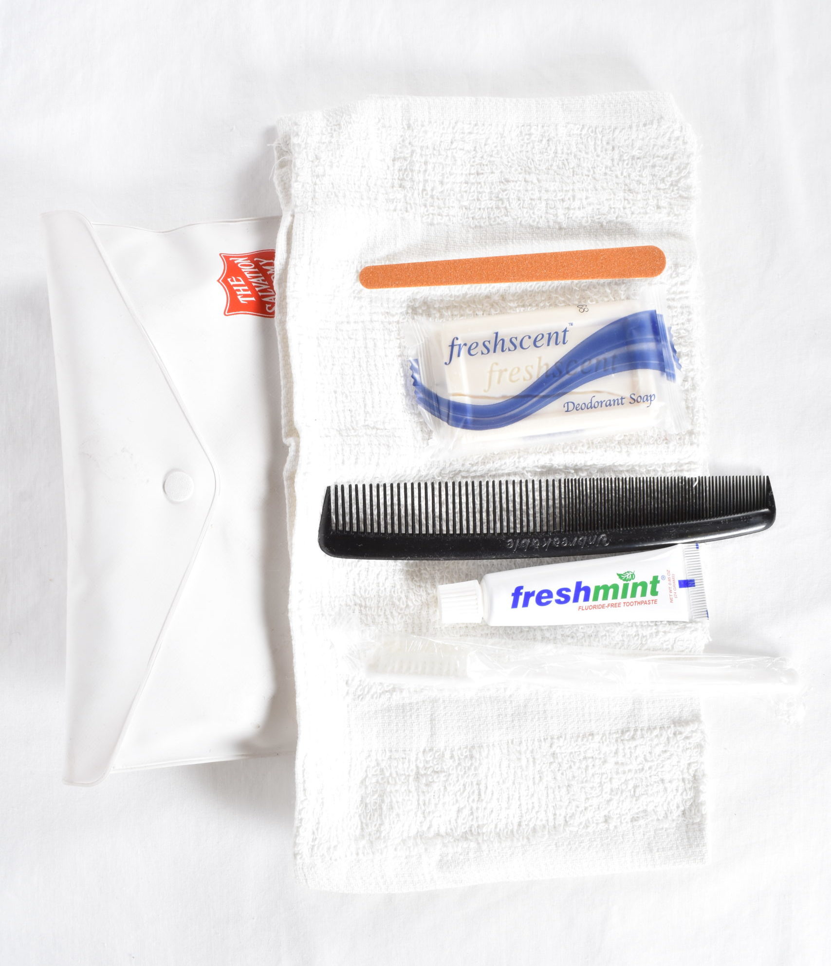 A hygiene kit with white wash cloth, white toothbrush, toothpaste, black comb, bar of soap, and nail file. The items are housed in a white vinyl envelope which closes with a snap.