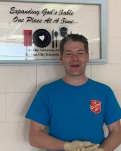 A man with short brown hair wearing a blue t-shirt with a Salvation Army Red Shield logo