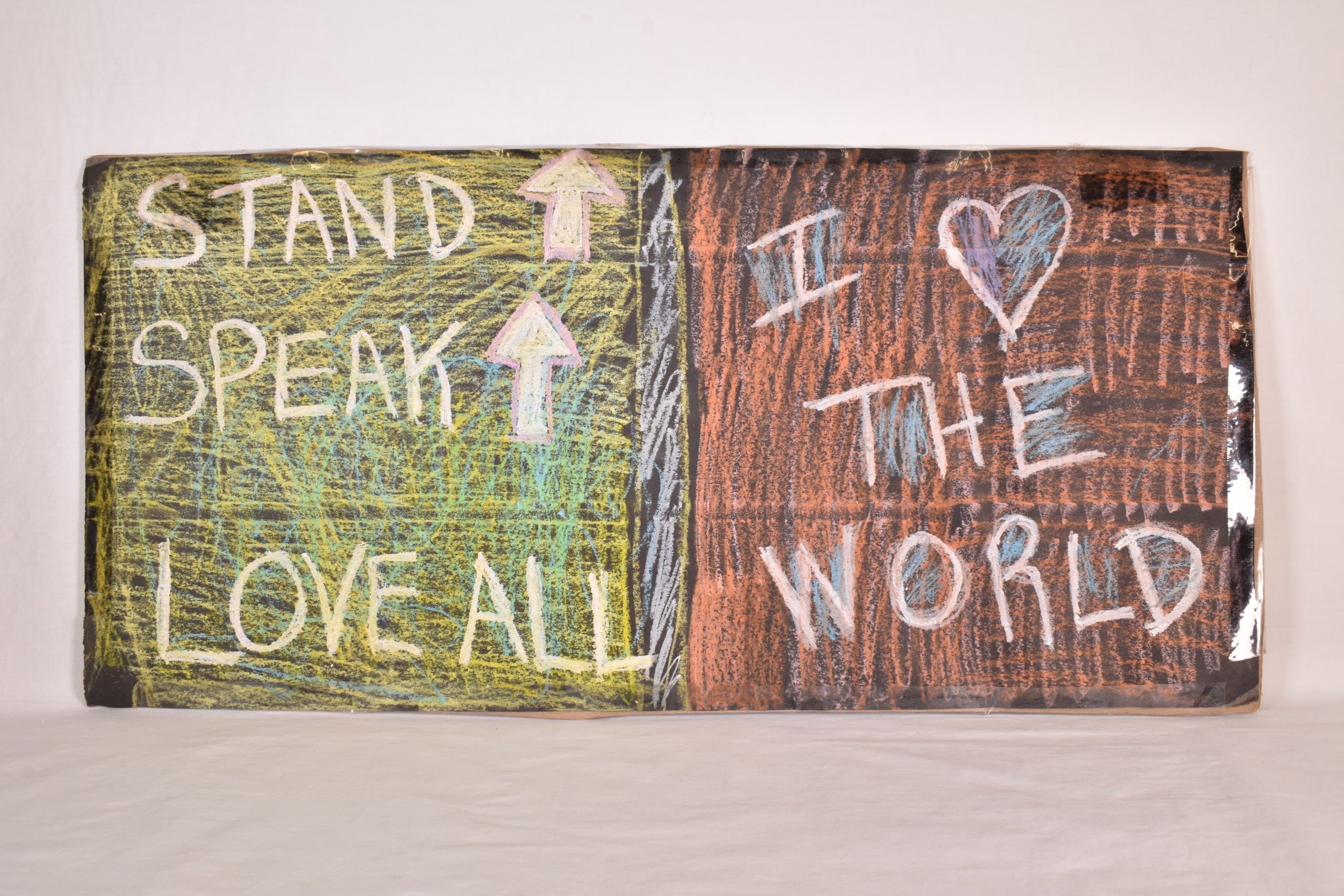 A hand colored sign which reads "Stand up (arrow pointing) Speak (arrow pointing up) Love All I (heart) the World