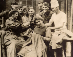 A group of soldiers poses with two Salvation Army female workers who are mending the soldiers uniforms.