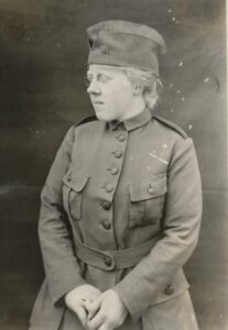 Black and white photograph showing a woman looking to the left of the screen. She wears a fabric military overseas cap and World War I style uniform.